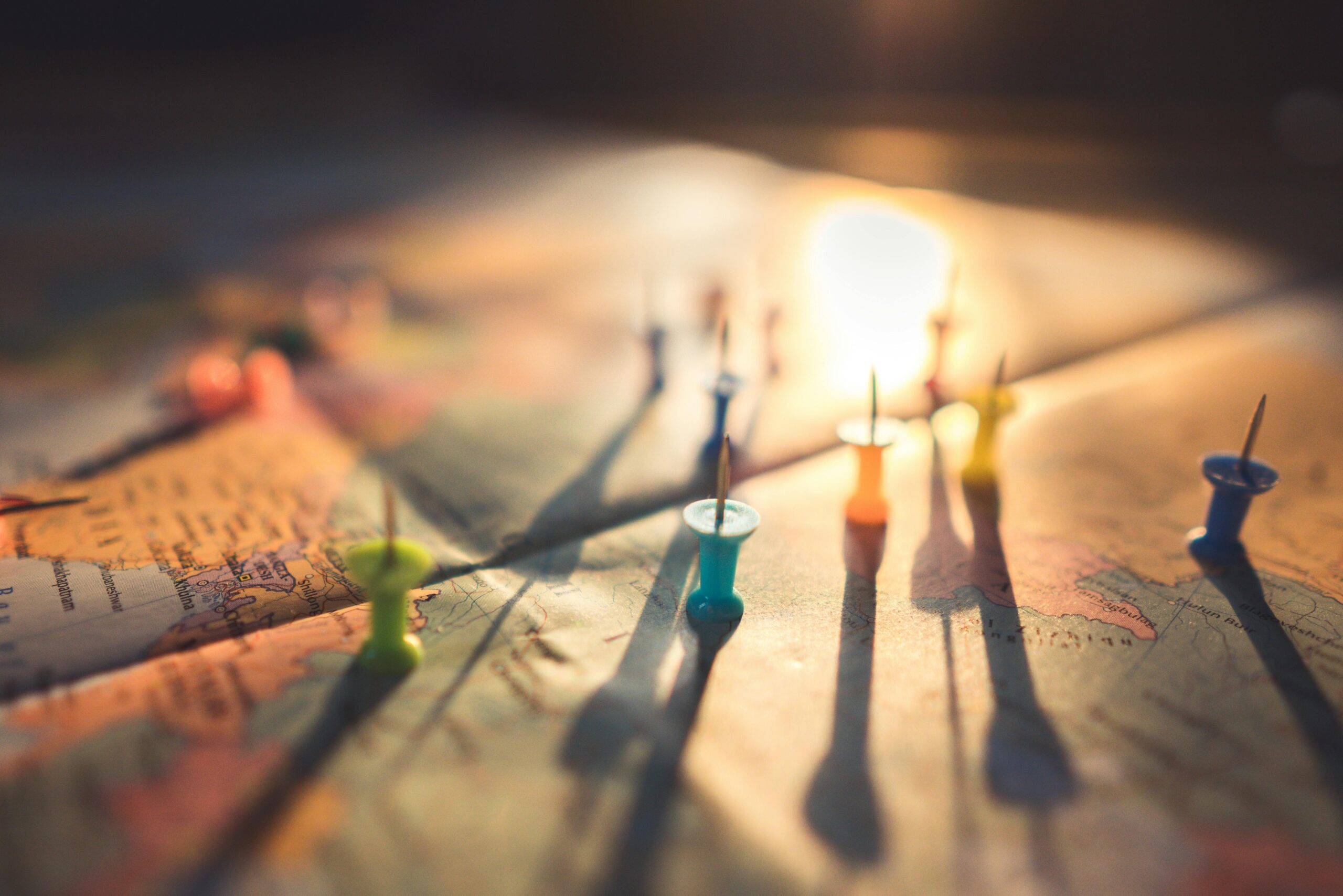 A close-up view of colorful push pins casting shadows on a world map during sunset, highlighting global travel.